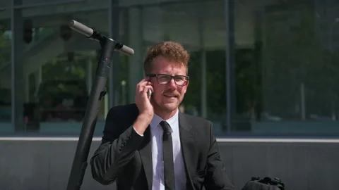 Office worker talking on cellphone sitting on electric scooter outdoors Stock Footage 143908785