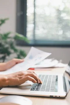 Office worker typing on laptop while reviewing documents, illustrating digi.. Stock Photos