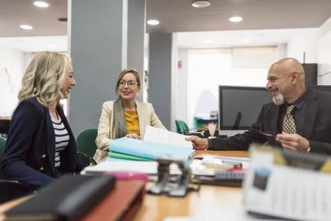 Office workes talking and looking files: women and mature boss at desk Stock-Fotos