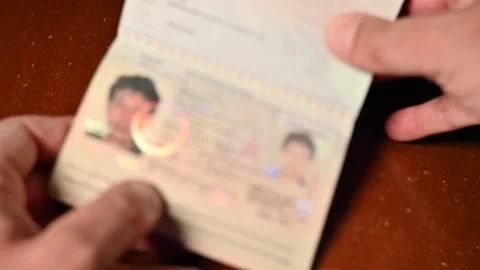 Officer hands checking leafing through blurred passport on wooden desk Stock Footage 154058644