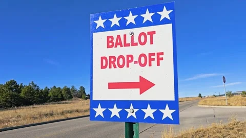 Official ballot drop-off direction sign stands beside a road with bold red Stock Footage 340866767