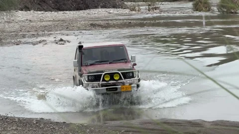 Offroading jeep crossing water stream by splashing water on an overcast day in Stock Footage 303475295