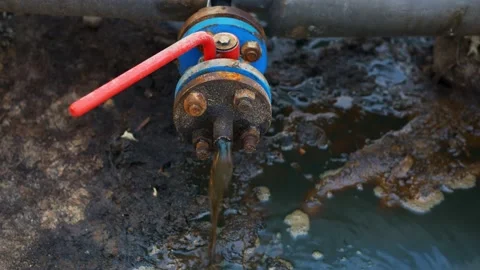 An oil and gas worker opens a tap from a pipe and crude oil begins to flow to Video stock 166273186