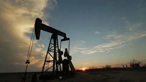 Oil derrick drill pump in the foreground of setting sun and blue sky A Stock Footage 125639124