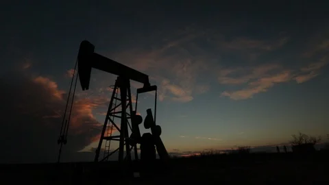 Oil derrick drill pump in the foreground of setting sun and blue sky B Video stock 125639151