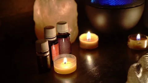Oil essentials next to electric diffuser lamp, candles on wooden table in room. Video stock 129298750