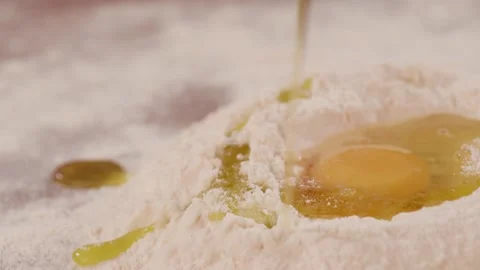 Oil flows down on flour and raw egg yolk. Pouring olive oil in the flour with Stock-Footage 151119348