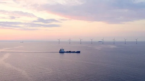 Oil products tanker sailing past offshore wind farm at sunrise. Stock Footage