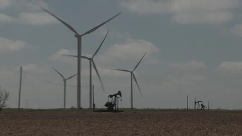 An oil pump jack - camera pulls back to reveal wind turbines, 4K. Stock Footage 232262862