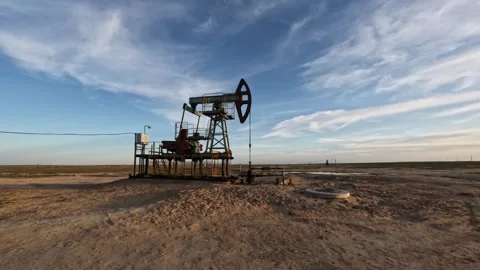 Oil pump jack operating in an open field under a clear blue sky Stock Footage 337725690