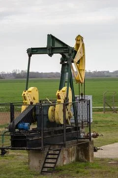 Oil Pump Jack Operating in Open Field With Clear Sky and Surrounding Landscap Stock Photos