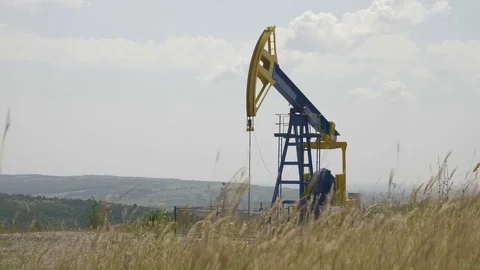 Oil pump working in the wheat field with hills in background Video stock 82179660