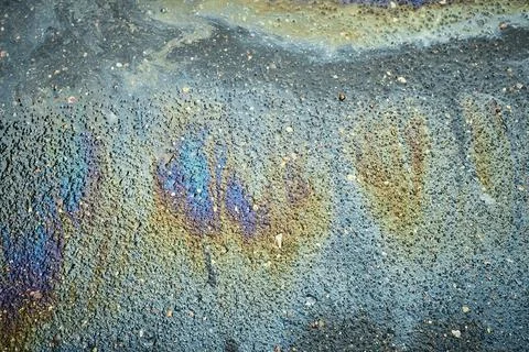 Oil slick on asphalt pavement surface forming colorful iridescent pattern and Stock Photos