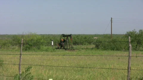 Oil well pumping through wire fence Stock Footage 502339