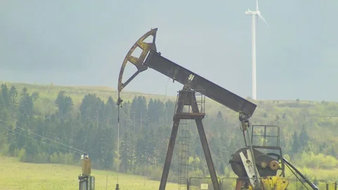 Oil well pumpjack and Wind power plant in background with gray sky Stock Footage 74791765
