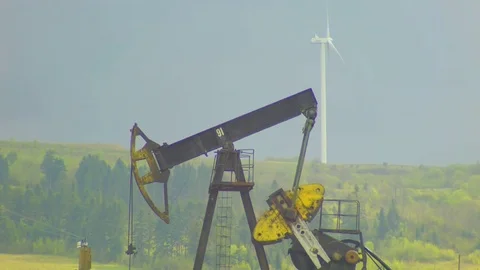 Oil well pumpjack and Wind power plant in background with gray sky Stock Footage 74791860