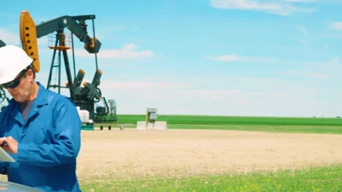 Oilfield worker using a tablet computer on location at oil field with pumpjacks Vidéo 163162434