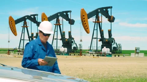 Oilfield worker using a tablet computer on location at oil field with pumpjacks Vidéo 163162451
