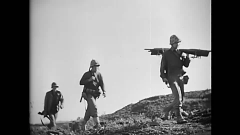 OKINAWA - 1945 - Shells explode, and a 37mm gun crew carries a gun up a hill in 動画素材 287744938