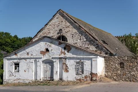 Old abandoned building with weathered plaster facade near stone wall in Ukrai Stockfoto's