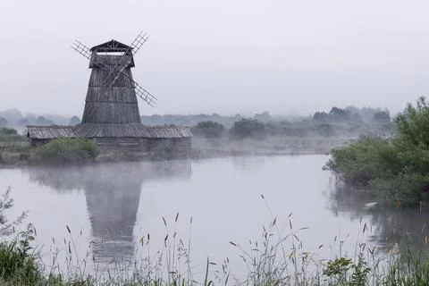 An old abandoned mill with a reflection on the river in the fog at dawn. Stock Photos