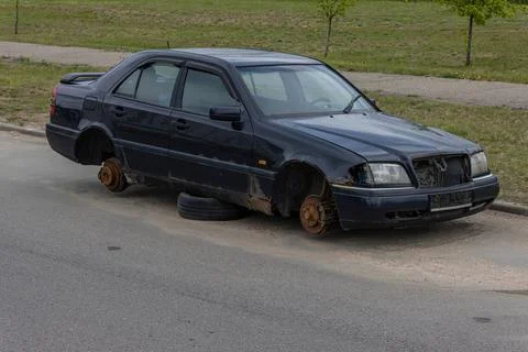 Old abandoned rusty car without wheels on the side of the road Stock Photos