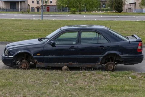 Old abandoned rusty car without wheels on the side of the road Stock Photos