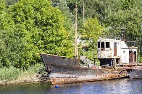 Old abandoned rusty small ship. Against the background of green overgrown tre Stock-Fotos