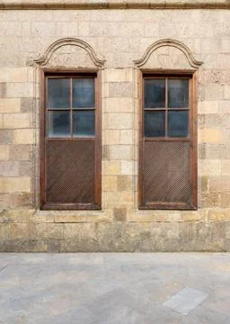 Old abandoned stone decorated bricks wall with two arched wooden shutter windows Stock Photos