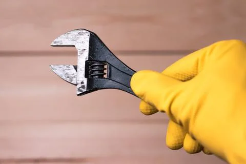 Old adjustable wrench in the hand of a worker in a glove. Stock Photos