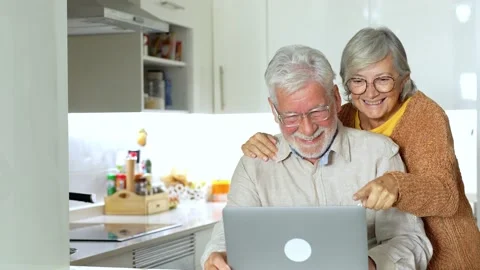 Old age and modern tech. Retired family couple sit at kitchen table use lap.. Stock-Footage 236928216