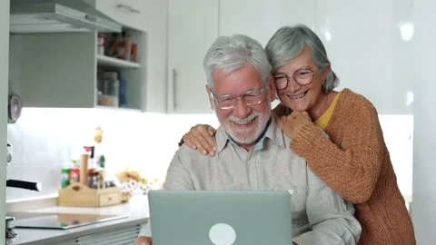 Old age and modern tech. Retired family couple sit at kitchen table use lap.. Stock Footage 236928413