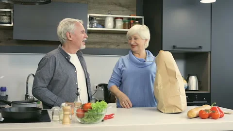 Old aged couple at the kitchen. Taking food from brown grocery bag. Stock Footage 102216441
