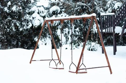 An old aged rusty iron double swing for children covered with snow in park Stock Photos