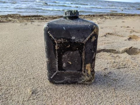 Old and plastic square black bottle on the sandy beach Foto stock