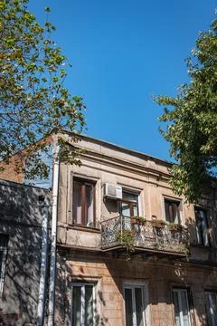 Old apartment building facade with a small balcony and a clear blue sky Stock Photos