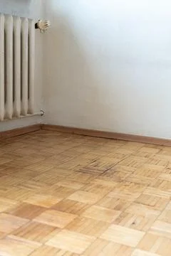 Old apartment interior with worn herringbone parquet floor and outdated radiator Stock Photos