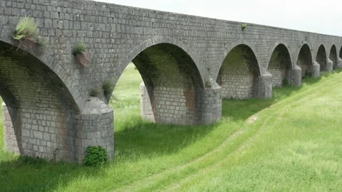Old arch bridge made of stone over a green grassy field - long vintage viaduct Stock Footage 211175757