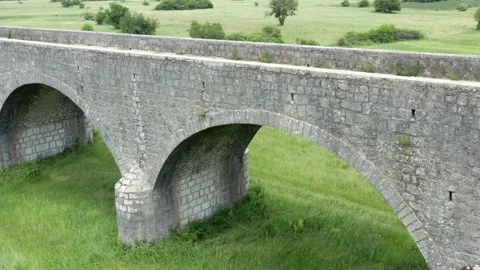 Old arch bridge made of stone over a green grassy field - long vintage viaduct Stock Footage 212153252