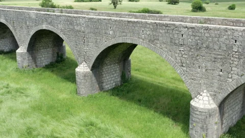 Old arch bridge made of stone over a green grassy field - long vintage viaduct Stock Footage 212166973