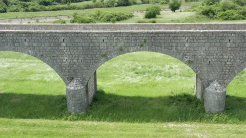 Old arch bridge made of stone over a green grassy field - long vintage viaduct Stock Footage 212181293