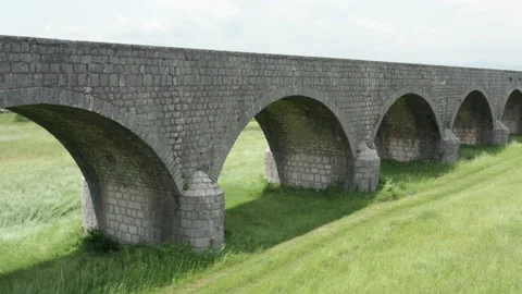 Old arch bridge made of stone over a green grassy field - long vintage viaduct Stock Footage 212196483