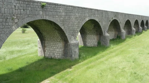 Old arch bridge made of stone over a green grassy field - long vintage viaduct Stock Footage 212205707