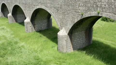 Old arch bridge made of stone over a green grassy field - long vintage viaduct Stock Footage 212213256