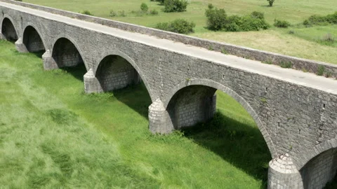 Old arch bridge made of stone over a green grassy field - long vintage viaduct Stock Footage 212229535