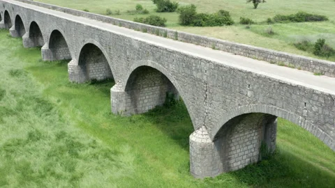 Old arch bridge made of stone over a green grassy field - long vintage viaduct Stock Footage 212237208