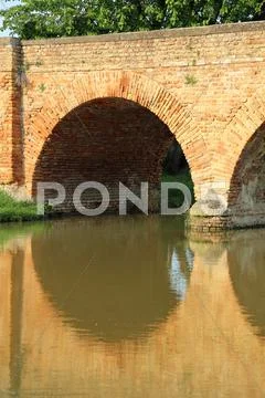 Old arched bridge made with red bricks with the river Stock Photos