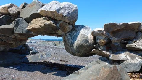 An old arched rock structure on a beach wedging a large rounded boulder. Stock Photos