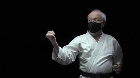 Old athlete performs blows and blocks with hands in a black medical mask Stock Footage 139145595