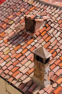 Old attic window and brick chimney on tile roof of a village house on sunny day Photos